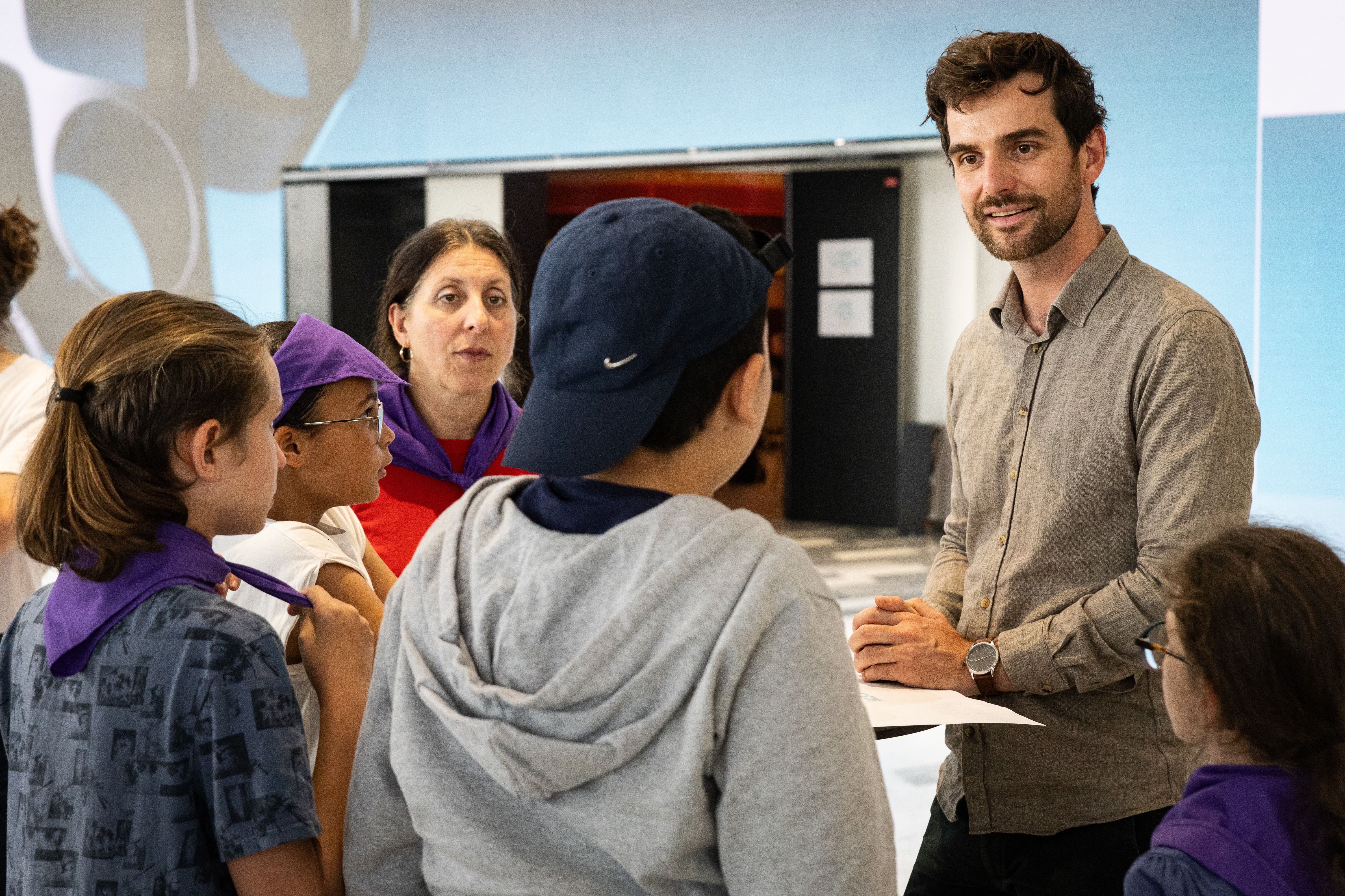 Speed Job Dating Yes We Code 2026 Un homme en chemise grise écoute et sourit à un groupe d'enfants de dos portant des foulards violets, dans le cadre d'une activité de speed job dating.